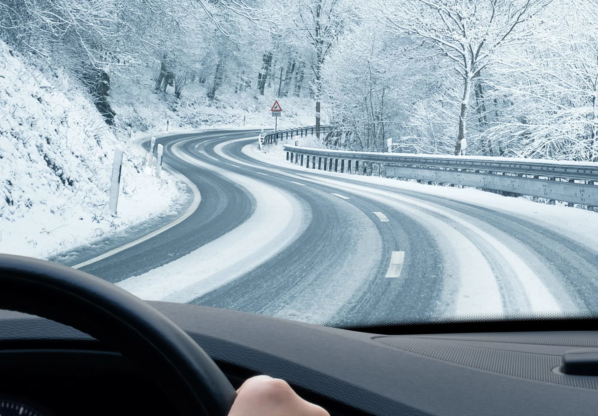 Vy från en bil som kör på en snöig och slingrande väg omgiven av snötäckta träd.