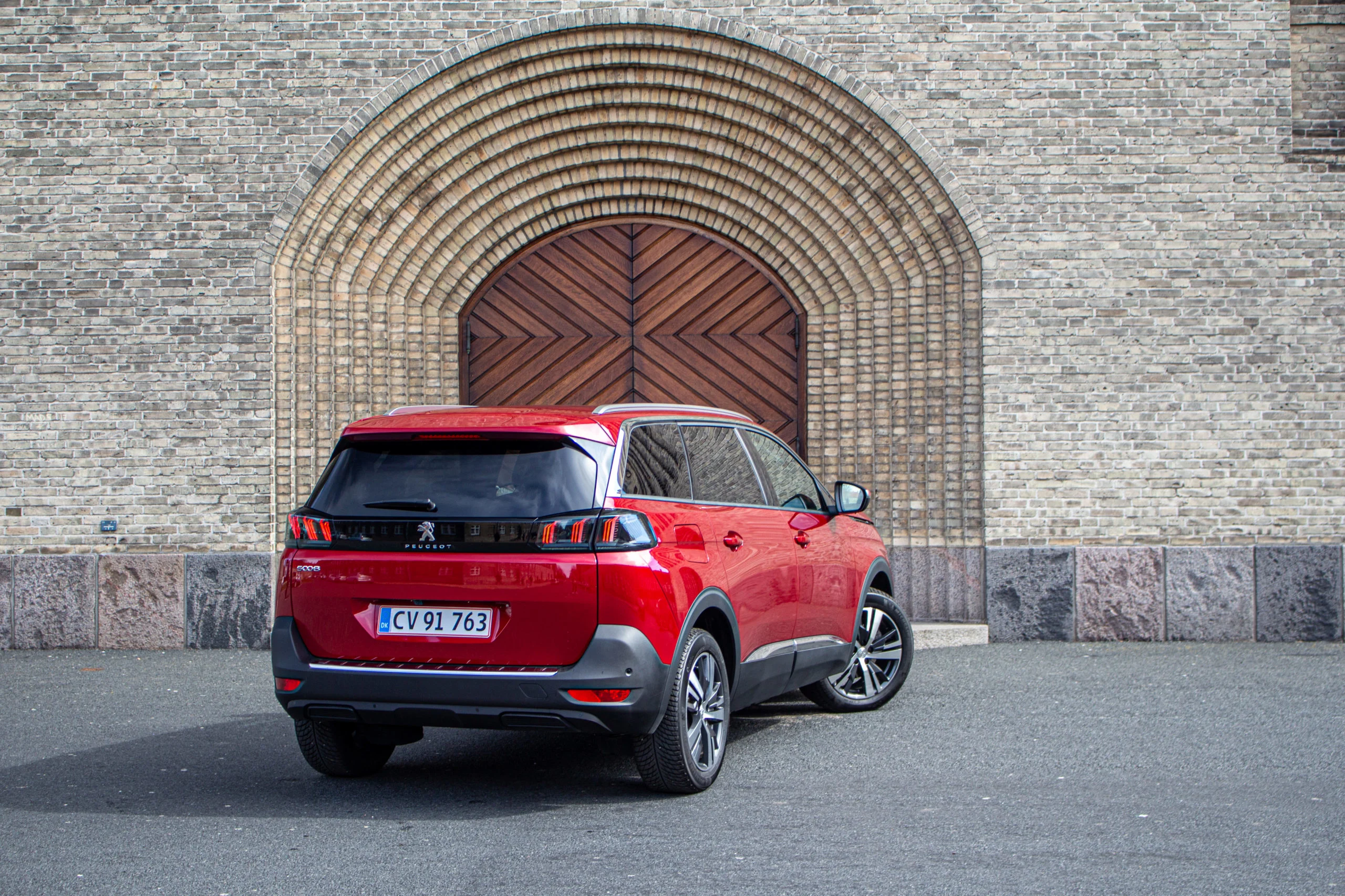 Röd Peugeot sedd bakifrån parkerad framför port i tegelbyggnad