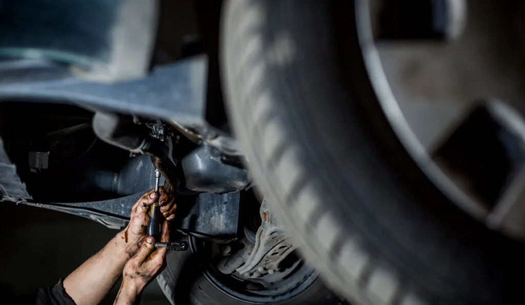Oljiga händer som skruver under bil