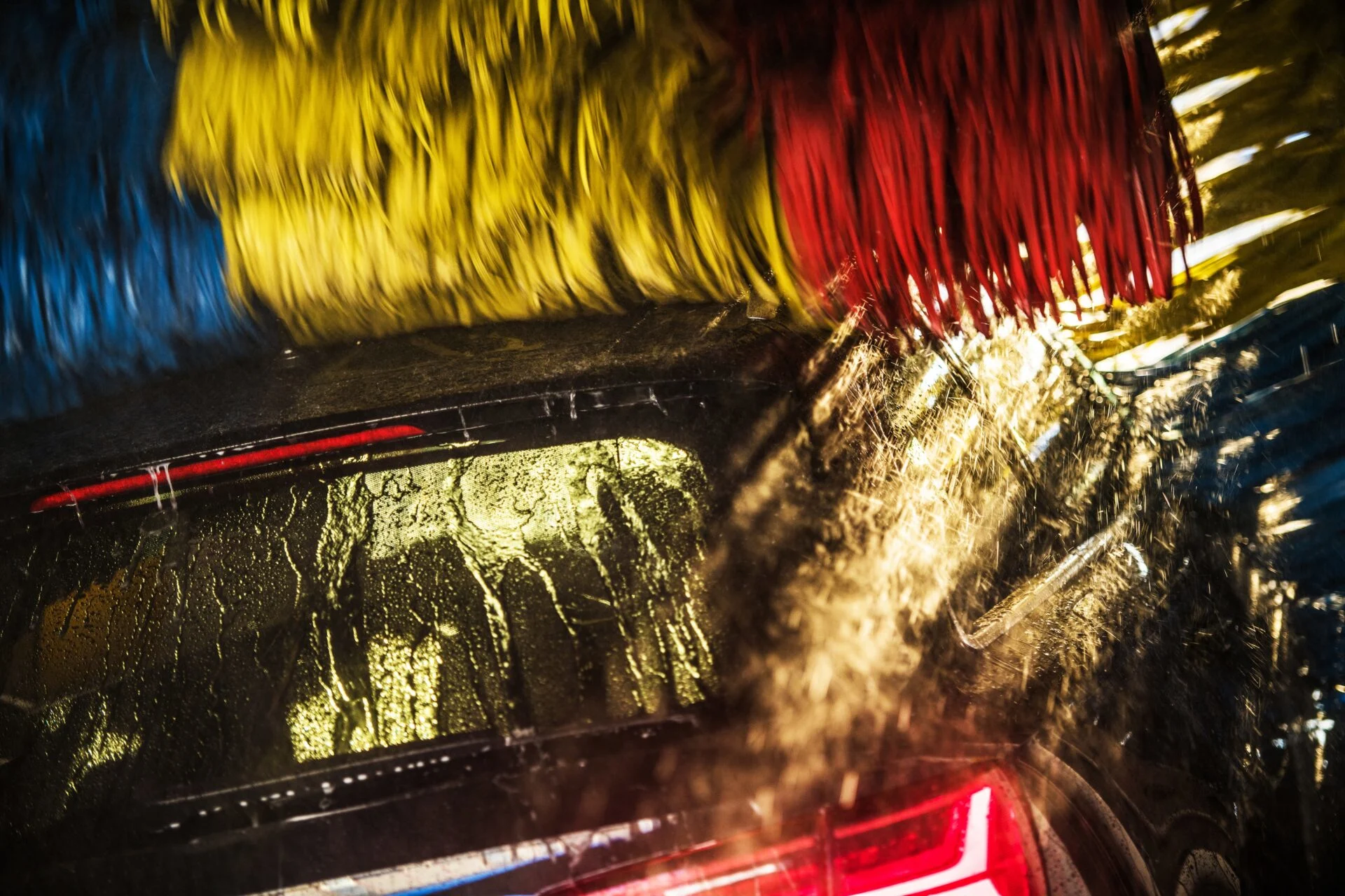 En bil i en automatisk biltvätt med färgglada borstar som rengör bakrutan