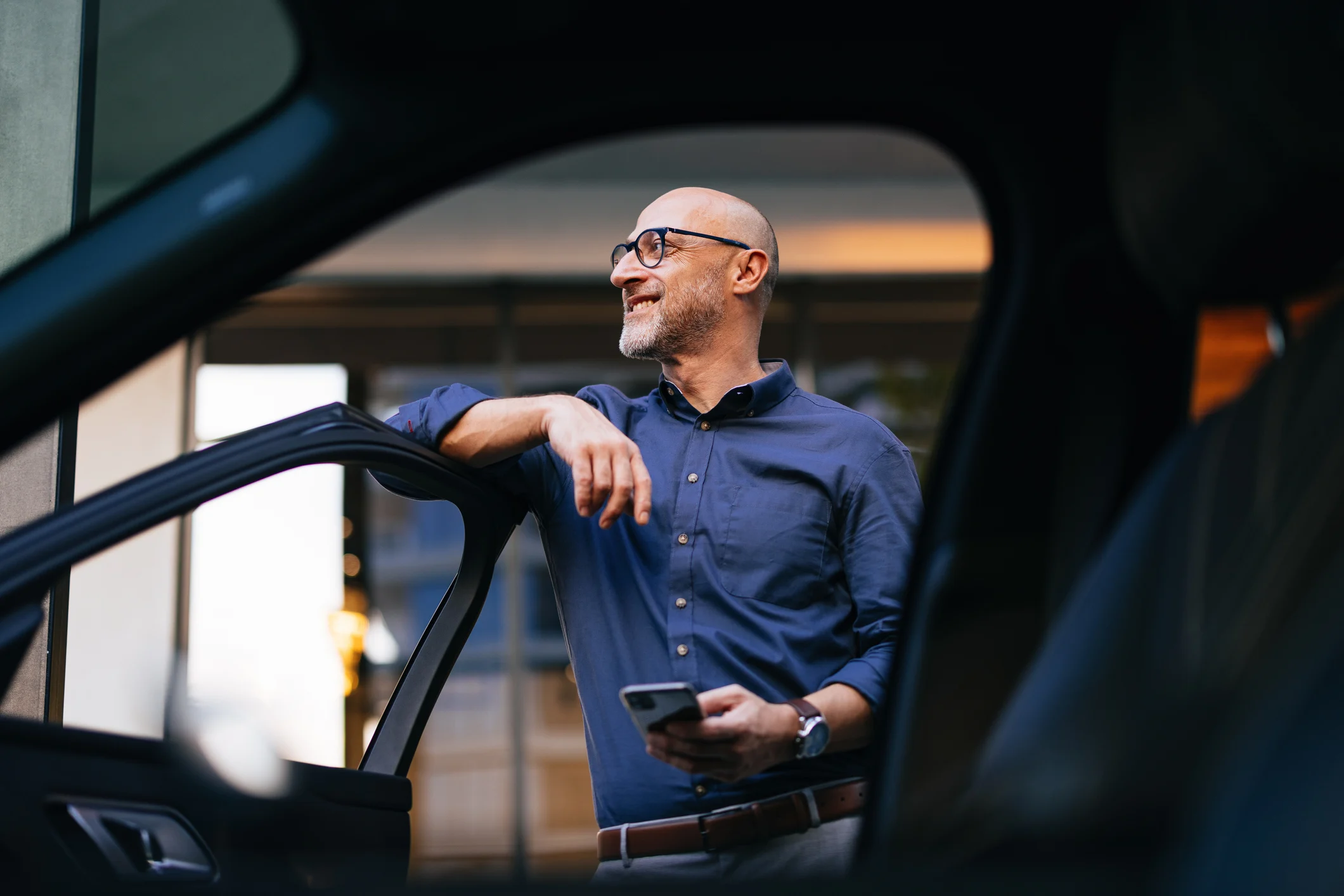 A man in a blue shirt viewed from the inside of a car with open door.