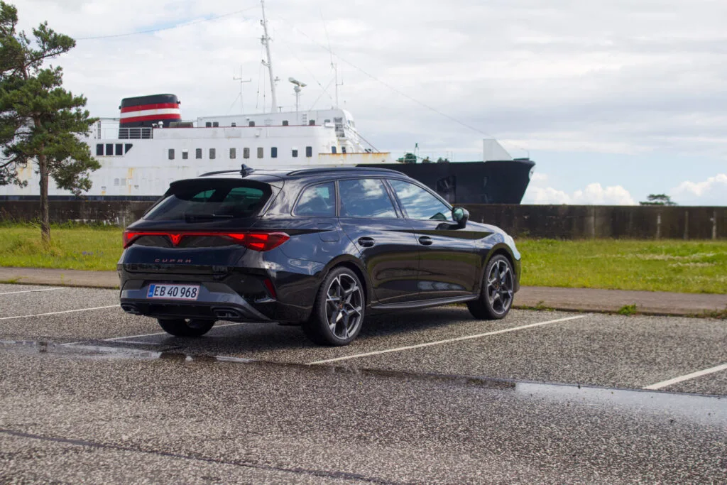 Parkerad Mörk Cupra Leon med färja i bakgrunden