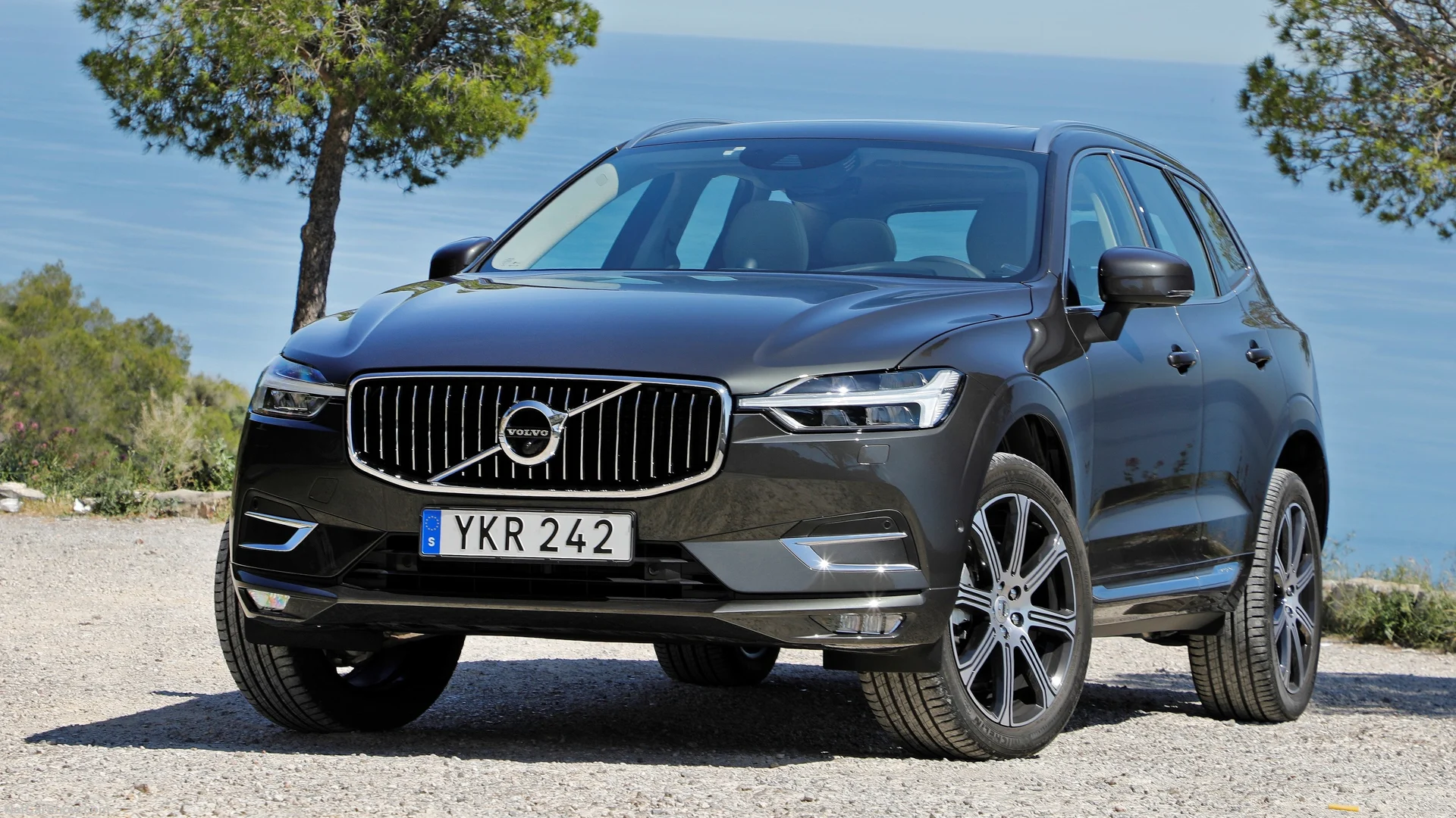Mörk Volvo XC60 parkerad med träd och hav i bakgrunden