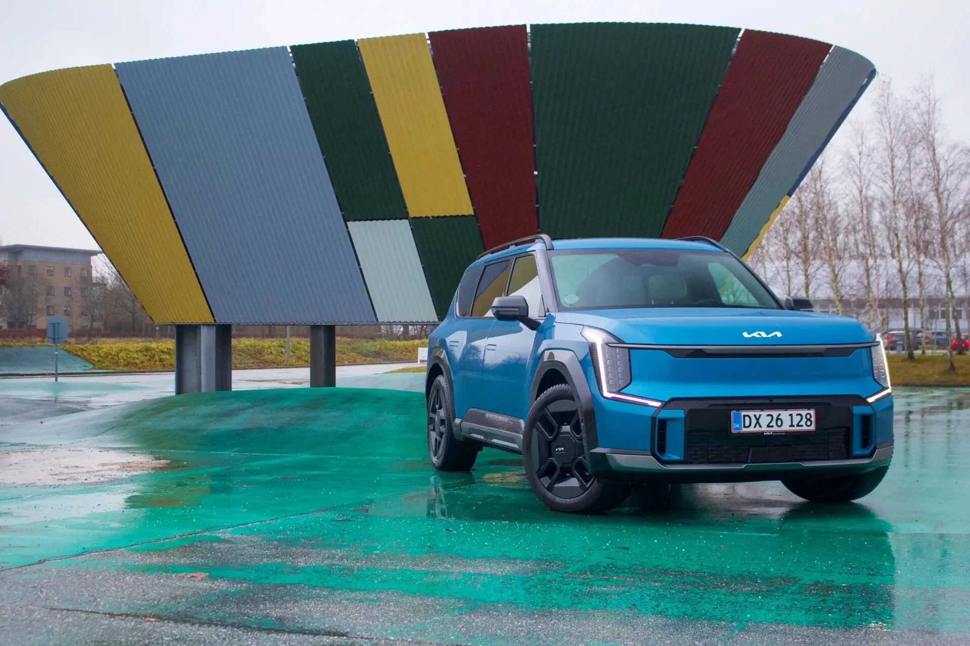 Blå Kia-EV9-GT-Line parkerad framför färggrant konstverk