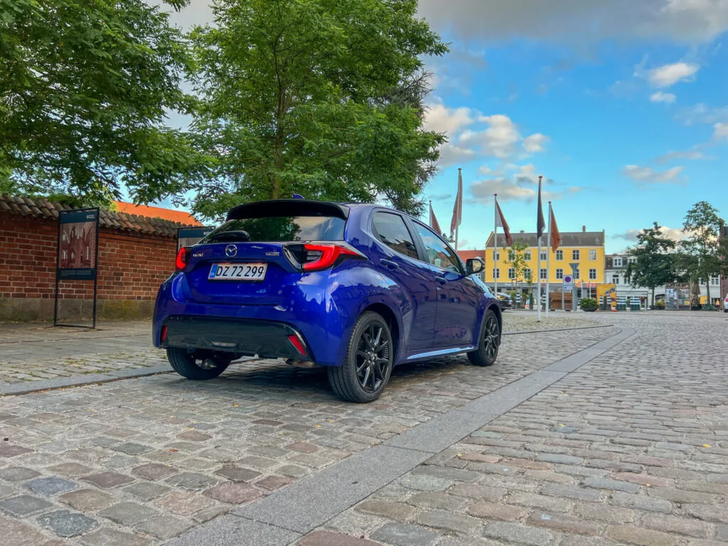 Blå Mazda 2 sedd bakifrån på kullersten