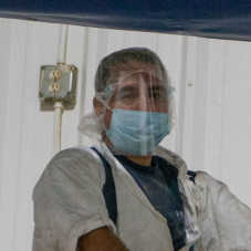 A masked Hearthside worker wearing a shiny clear facemask, standing in front of a power outlet