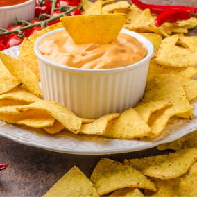 A plate of golden chips surround a single bowl of cheese dip