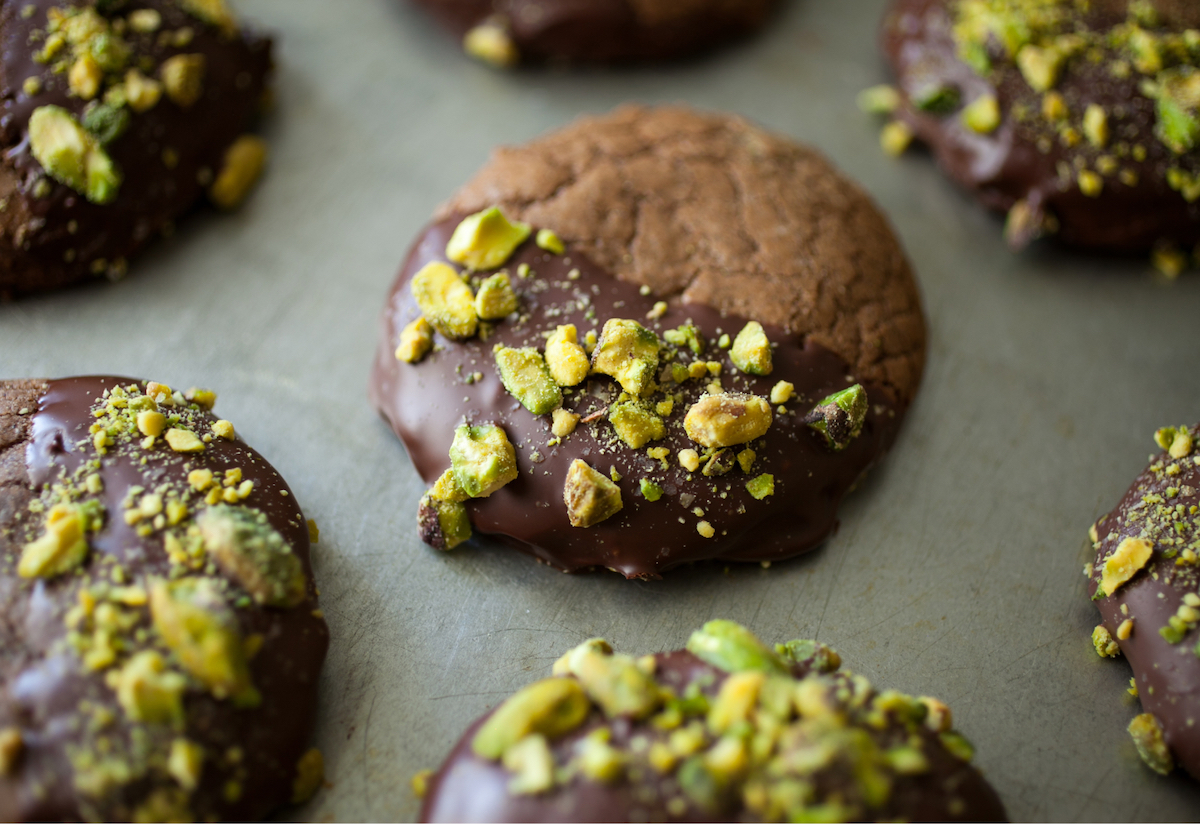 Chocolate-dipped pistachio cookies on a green-grey backdrop