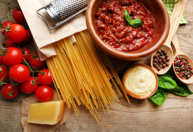Pasta sauce with raw noodles, tomatoes and cheese on a wooden backdrop