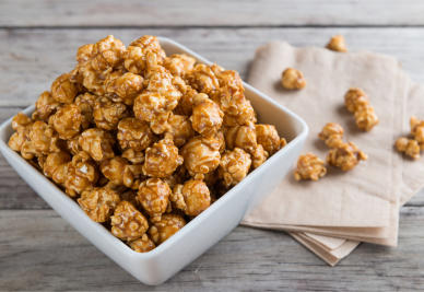 A bowl of caramel popcorn, with kernels overflowing onto brown napkins