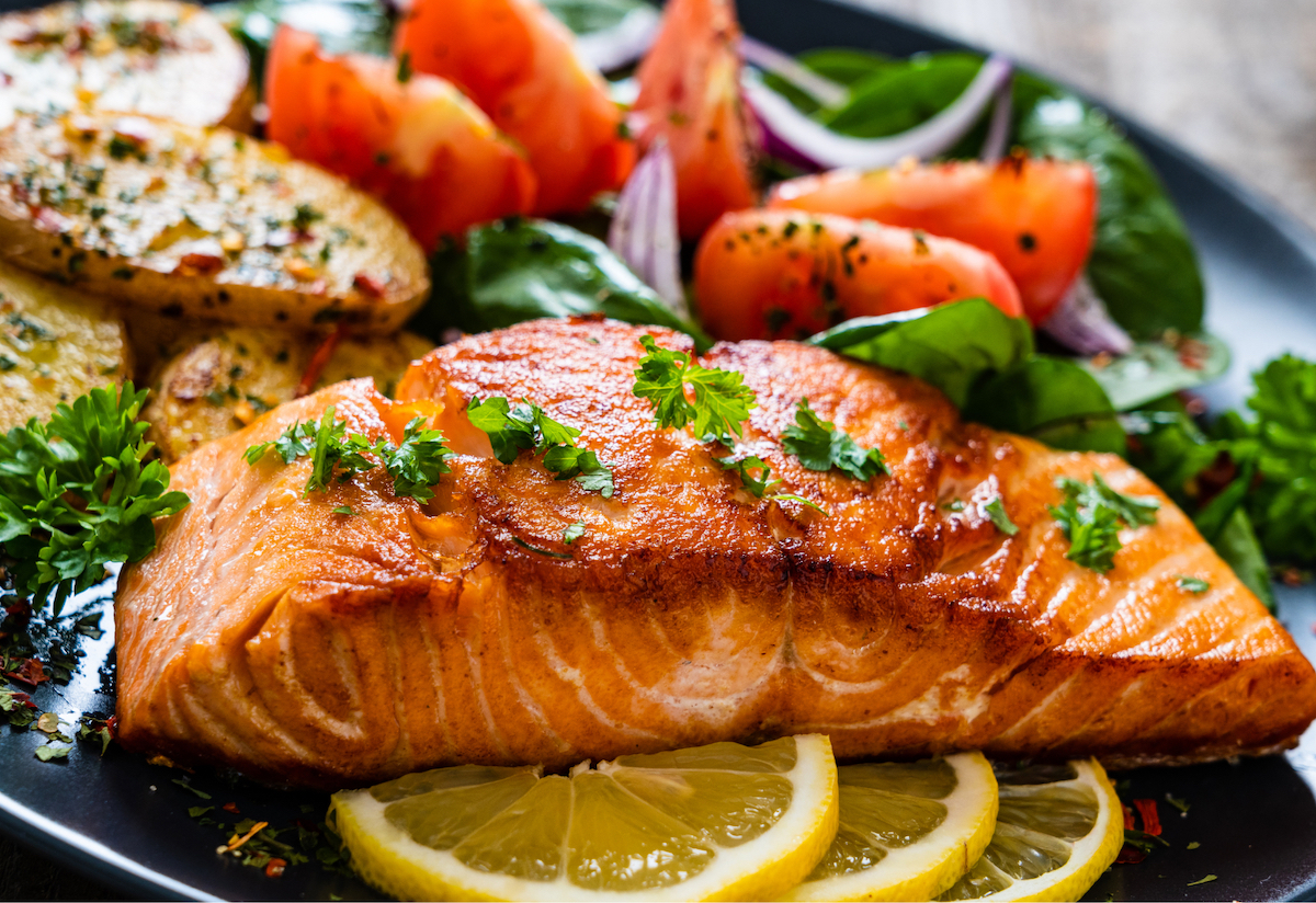 Freshly-cooked salmon on a plate with lemon slices, peppered tomato and potato wedges
