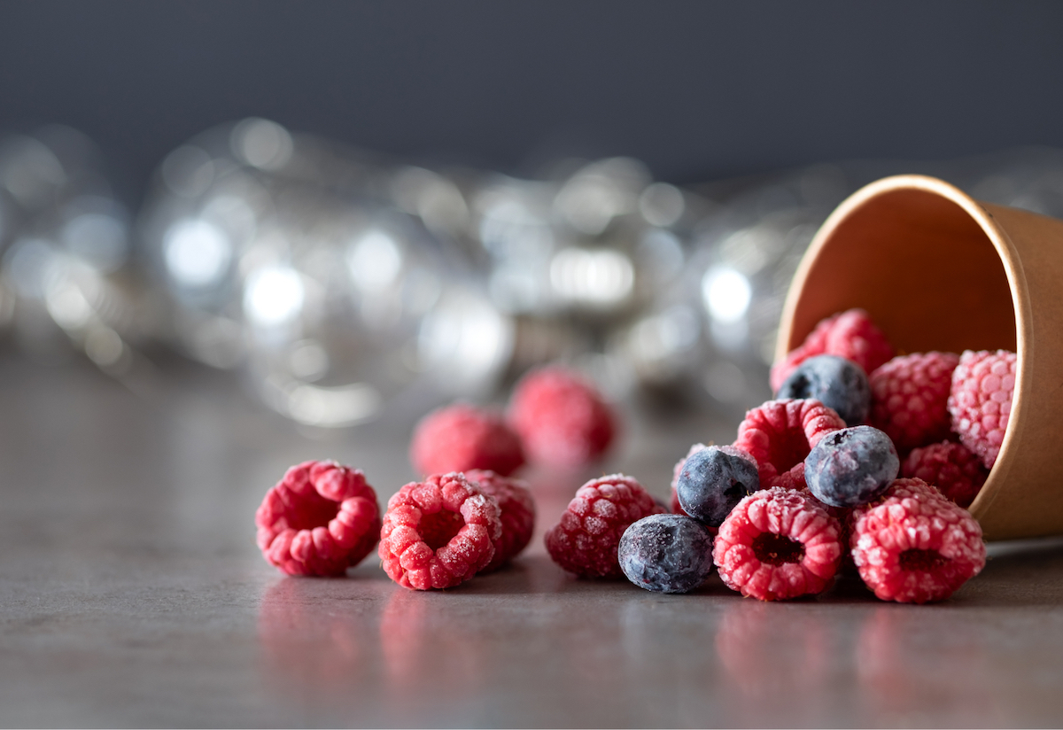 Frozen raspberries and blueberries fall from a brown cup onto a shiny surface