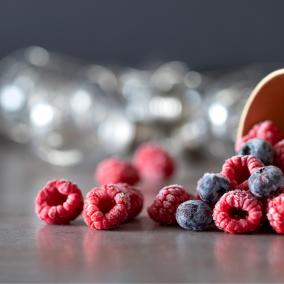 Frozen raspberries and blueberries fall from a brown cup onto a shiny surface