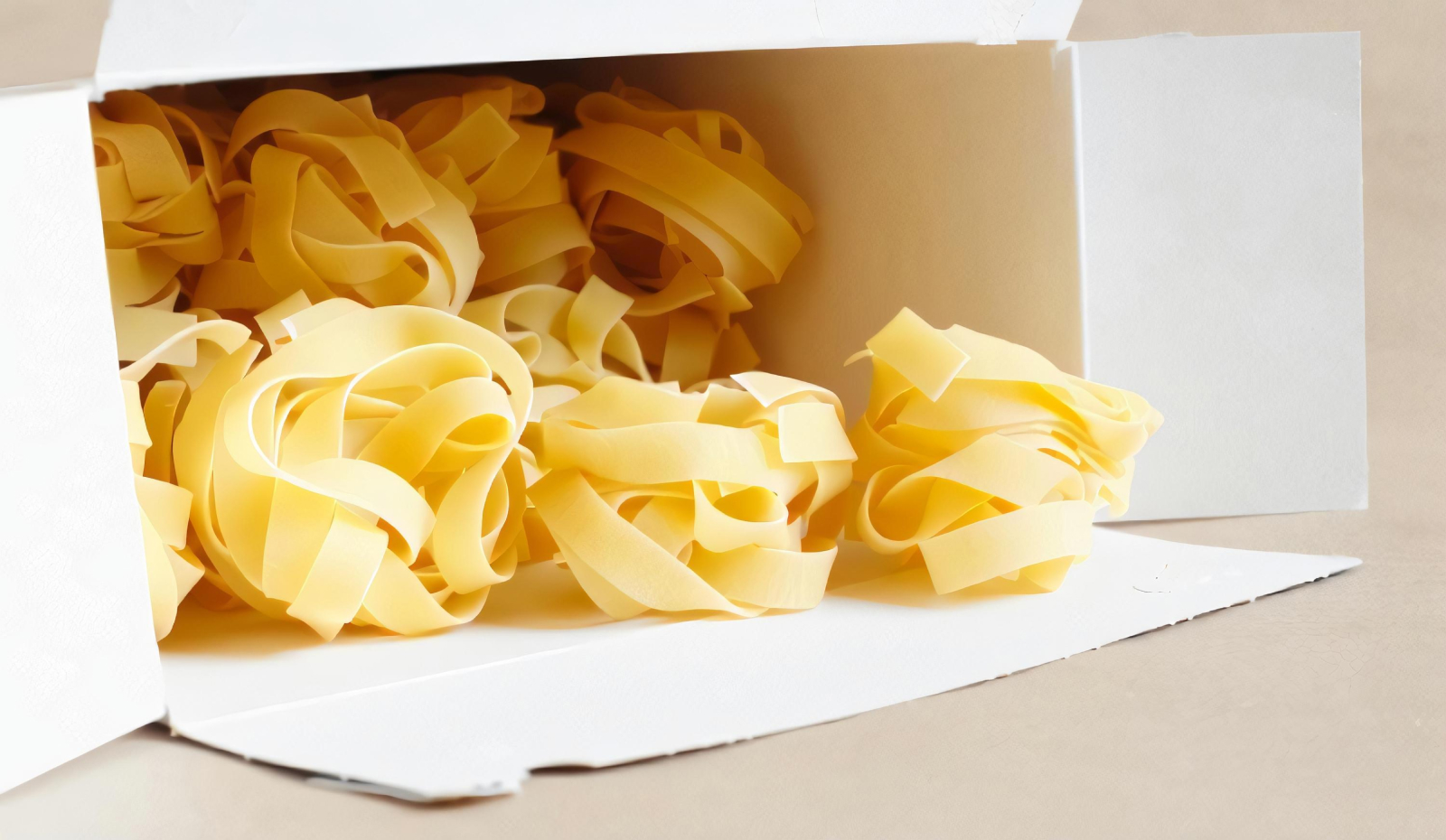 An open white carton overflows with fresh pasta noodles