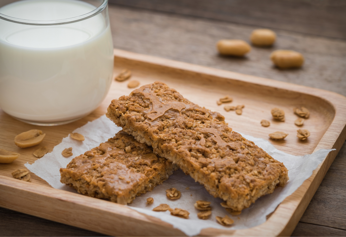 Two sweet crunchy bars sit on a wooden platter with a cold glass of milk