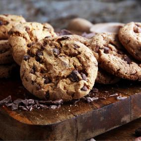 A plate of wire-cut chocolate chunk cookies, sitting on a thick wooden platter.
