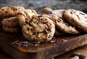 A plate of wire-cut chocolate chunk cookies, sitting on a thick wooden platter.