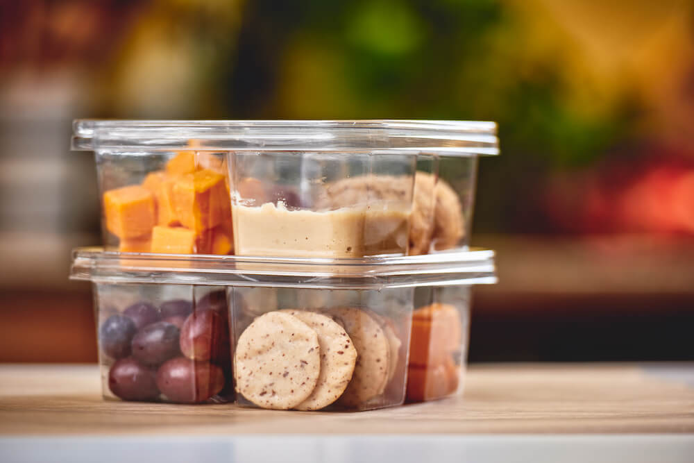 Cheese, dipping sauce, grapes, and crackers in clear plastic containers