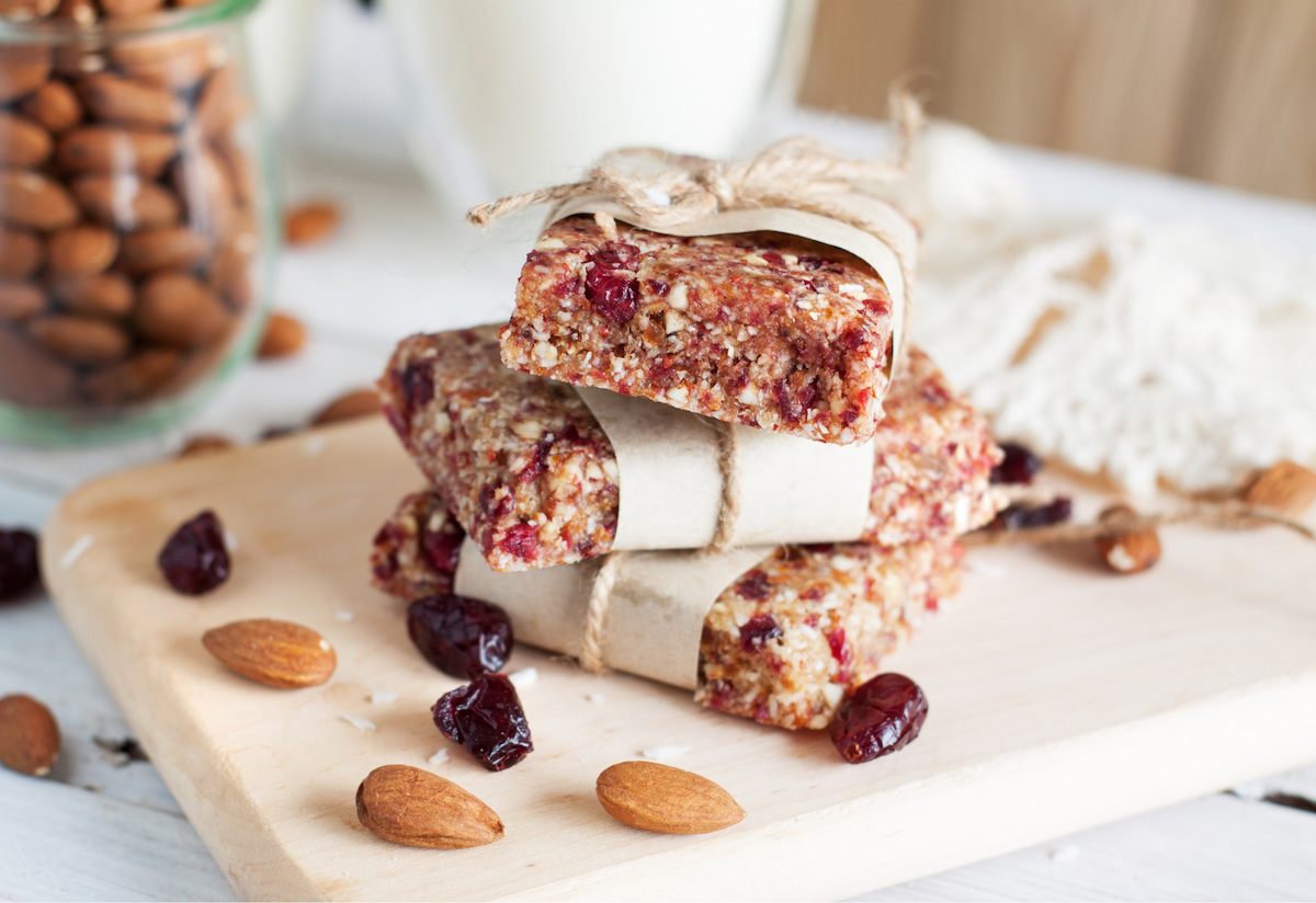 A stack of healthy energy bars, partially-wrapped in paper and twine, surrounded by almonds and dried berries