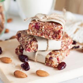 A stack of healthy energy bars, partially-wrapped in paper and twine, surrounded by almonds and dried berries