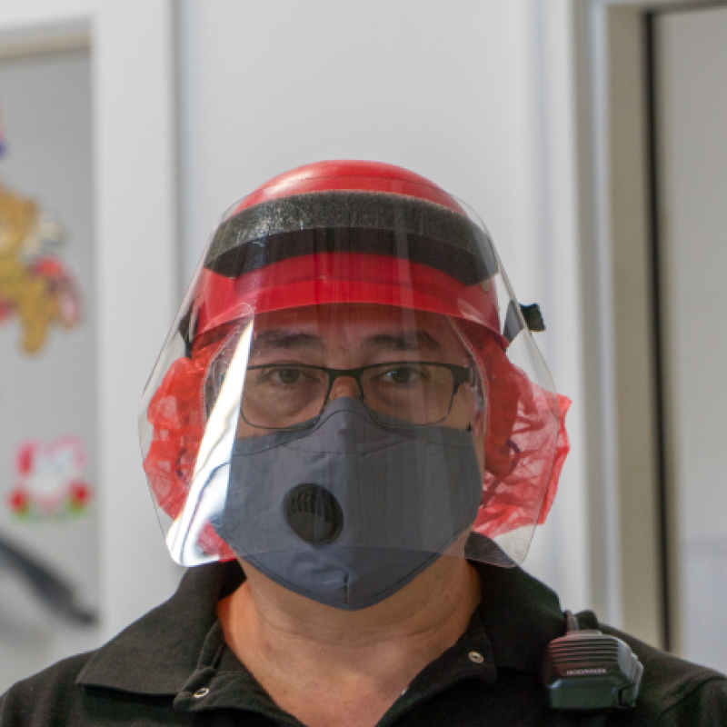 A masked Hearthside worker wearing a red hat and plastic face shield