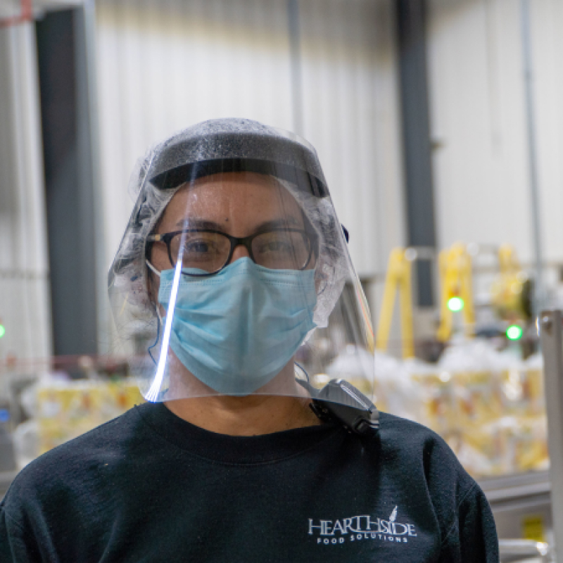 A masked Hearthside worker with a face shield and blue Hearthside shirt