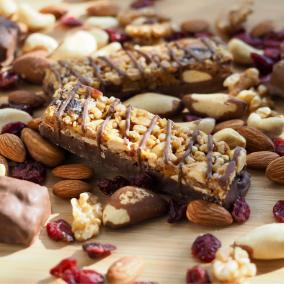 A chocolate-drizzled multi-layer bar on a bed of almonds and mixed nuts