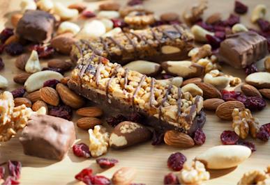 A chocolate-drizzled multi-layer bar on a bed of almonds and mixed nuts