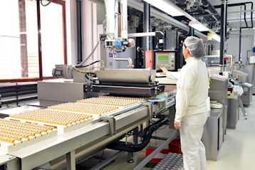 A woman wearing white monitors a conveyor belt.
