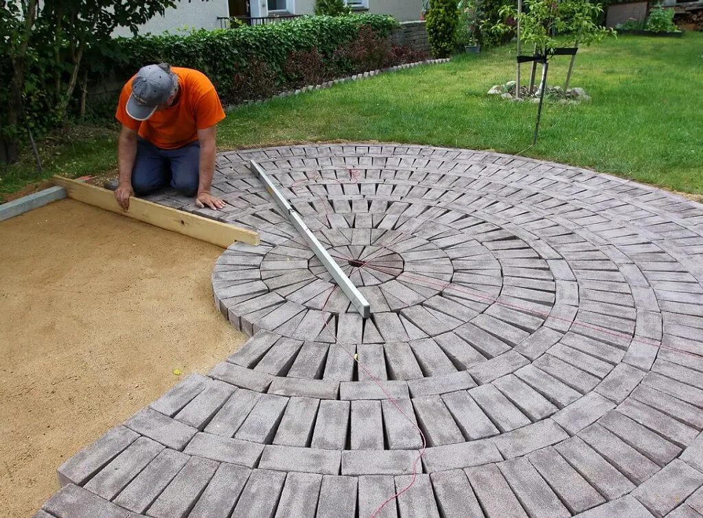 https://www.checkatrade.com/blog/wp-content/uploads/2021/07/paver-laying-slabs-in-garden-1.jpeg