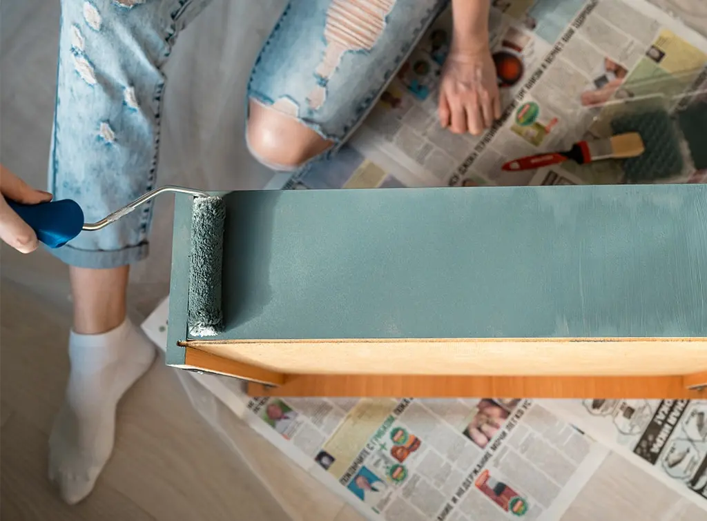 foam roller apply green paint to a piece of furniture