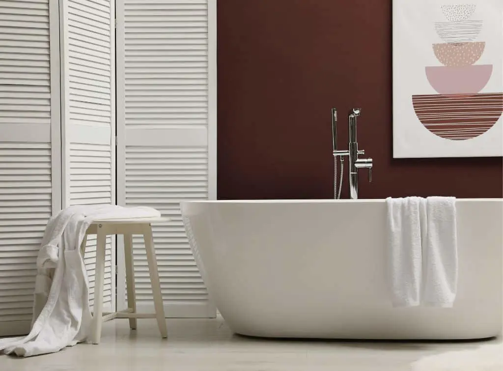 White bath, stool, and room divider with burgundy feature wall and matching artwork