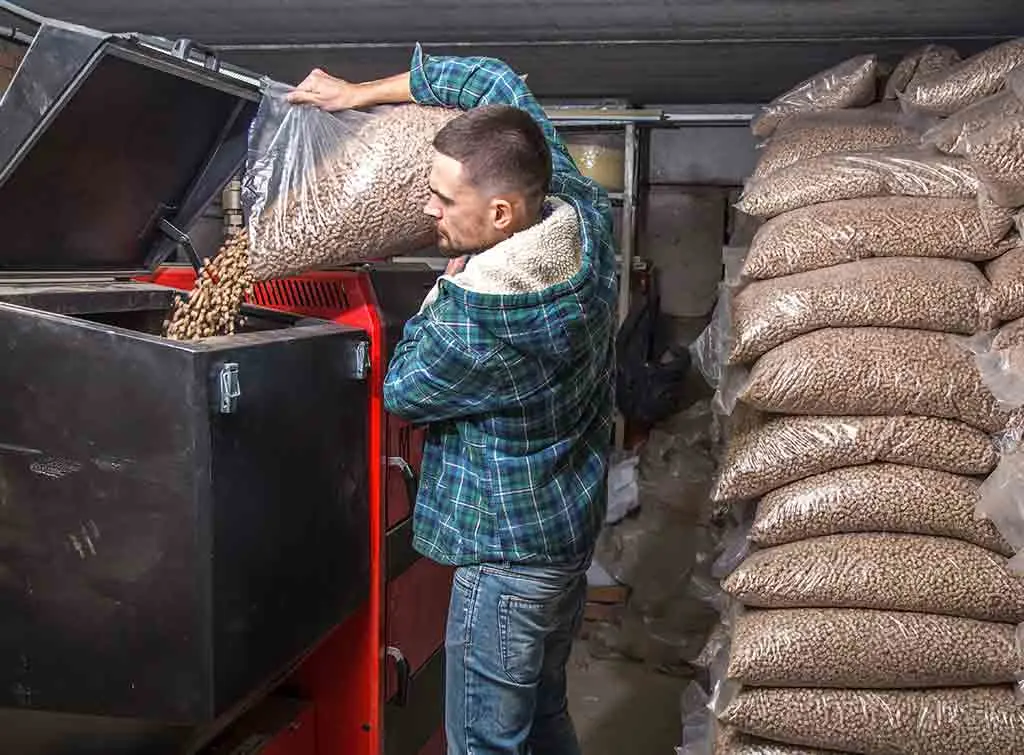 Engineer pouring pellets into biomass boiler. Central heating installers near me
