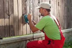 Man sanding a fence in preparation of painting it
