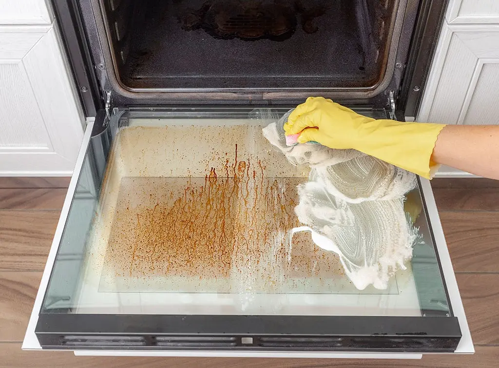 A person with rubber gloves on cleaning an oven door