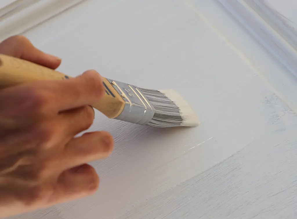 Top coat of paint being applied over primer on painted furniture