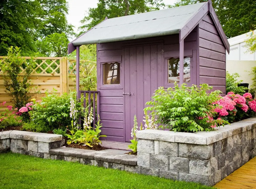 Pretty purple she shed idea with plants and brick border wall