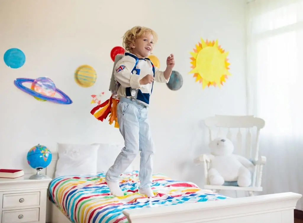 Young boy jumping up and down on his space-themed bed