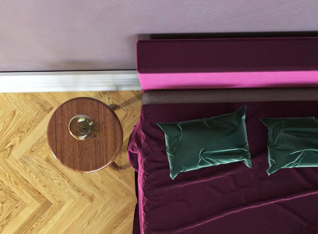 Birdseye view of velvet green cushions on a burgundy bedspread with wooden chevron floor tiles