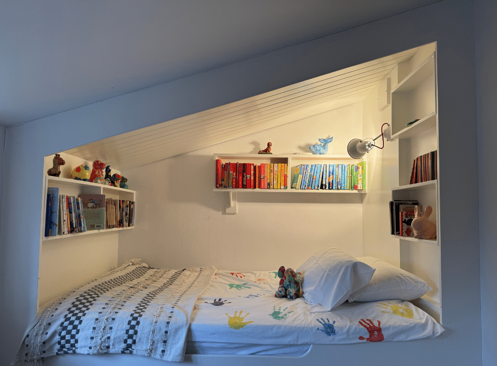 In the House with the Blue Shutters, a wall-mounted light above the raised bed makes for a cosy reading nook at bedtime