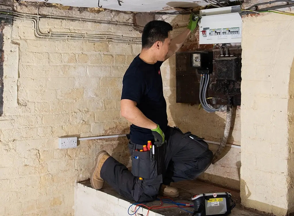 https://www.checkatrade.com/blog/wp-content/uploads/2024/07/electrician-work-trousers-in-use-with-fusebox.jpg