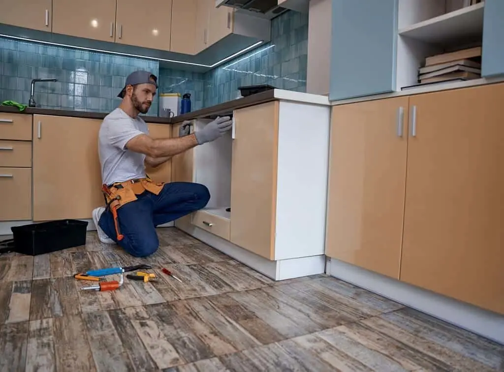 https://www.checkatrade.com/blog/wp-content/uploads/2024/12/handyperson-working-in-kitchen-with-doors.jpeg