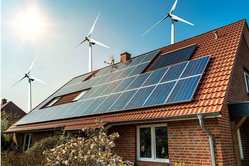 Home with solar panels on the roof and wind turbines in the background. Blog for Green home improvement grants - how to make your home more eco friendly