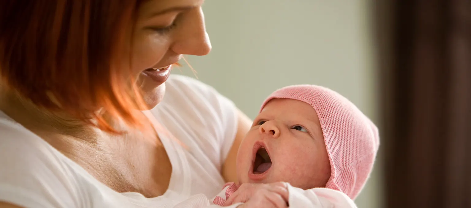 Mother holding and talking to baby in a pink hat