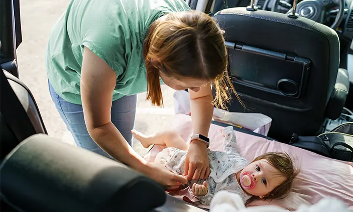 A mom is changing the diaper on the car seat.