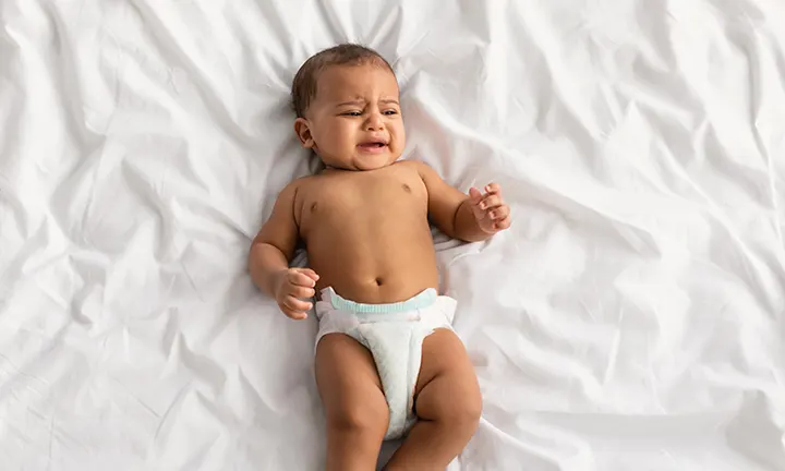 Baby lying on a white sheet, looking uncomfortable, possibly due to perianal strep infection in the diaper area.