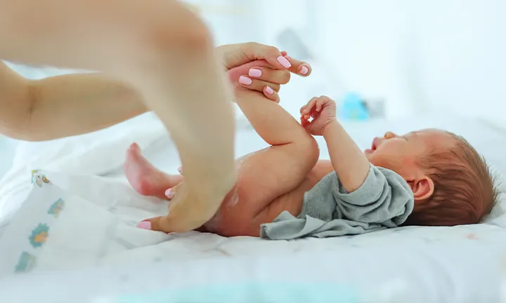 Parent changing a baby's diaper, using gentle care, as part of a home remedy for diaper rash.