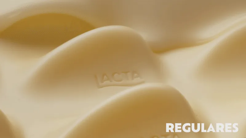 Close-up de ondas de chocolate branco Lacta derretido, exibindo textura cremosa com o logo da marca em relevo e o texto Regulares no canto inferior.