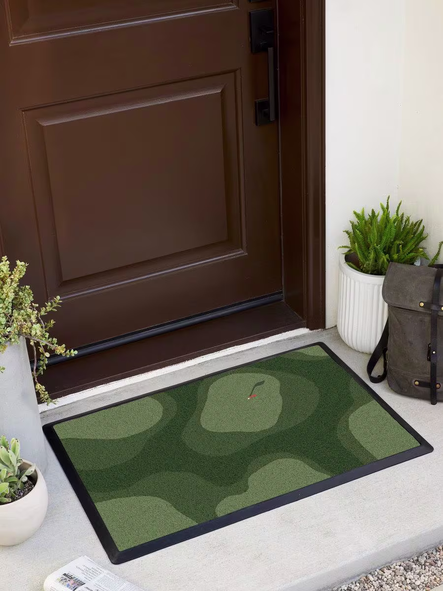 Ruggable Tee Time Doormat featuring overhead golf course illustration on front porch with wooden door, concrete planters, newspaper and leather backpack