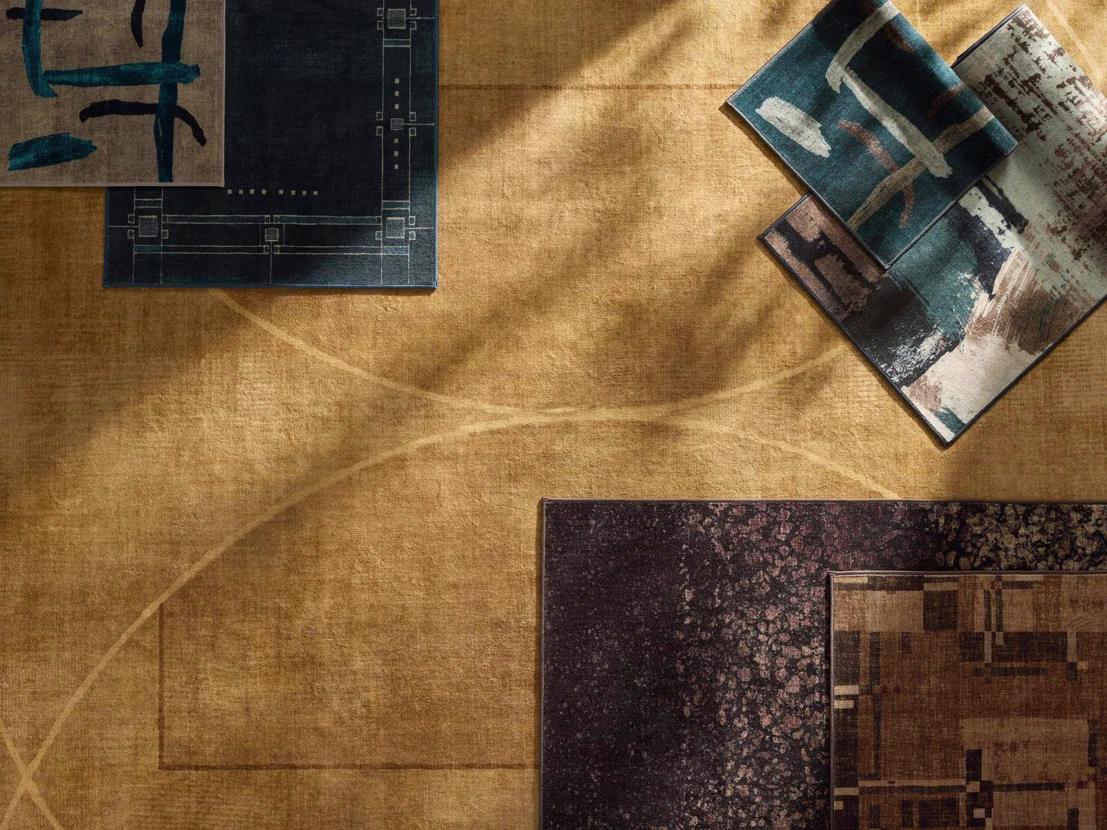 Image of multiple Ruggable x Architectural Digest rugs layered on top of one another showcasing colors of gold, deep blue, browns, and deep maroon. 